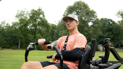 Person sitting on a lawn mower in a grassy area with trees in the background
